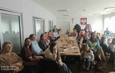 Przy stołach na białej sali siedzą licznie rodzice i ich dzieci oglądając nagrania filmowe i muzyczne dzieci.