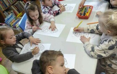 Dzieci przy stole kolorują pisanki.