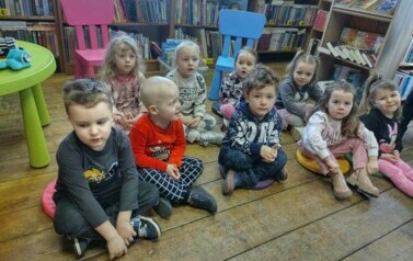 Na siedziskach siedzą dzieci i słuchają bajki czytanej przez bibliotekarkę.