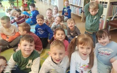 Na dywanie siedzą dzieci i słuchają bajki czytanej przez bibliotekarkę.