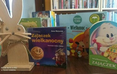 Na stole stoją drewnaine zajączki i świąteczne bajki.