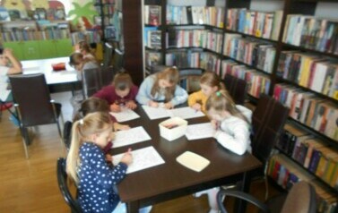 Dzieci siedzą przy stołach i robią karty pracy.