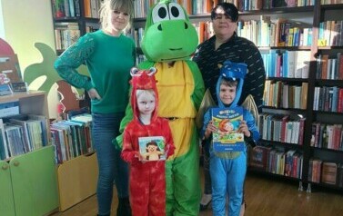 Trzy smoki w przebraniu stoją z Panią Anią i z bibliotekarką. Małe smoki trzymają książeczki.