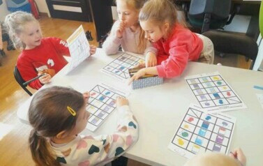 Dziewczynki przy stole uzupełniają karty pracy o książce.