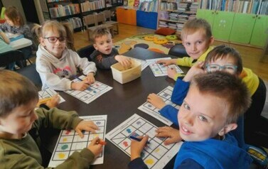 Dzieci siedzą przy stole i robią karty pracy o książce.