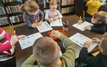 Dzieci siedzą przy stole i robią karty pracy o ekologii.