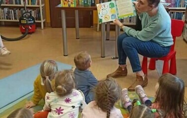 Dzieci siedzą na dywanie,a z przodu jedna z Pań z Przedszkola czyta im bajkę pokazując wnętrze książki.