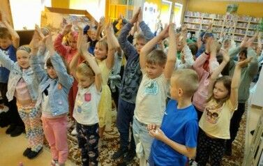 Duża grupa dzieci stoi z podniesionymi rękami do g&oacute;ry naśladując Pirata.