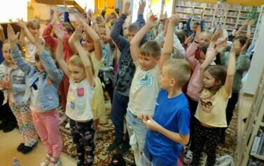 Duża grupa dzieci stoi z podniesionymi rękami do g&oacute;ry naśladując Pirata.