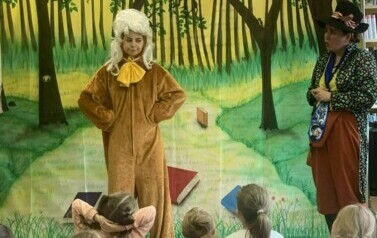 Na tle lasu stoi dw&oacute;ch przebranych aktor&oacute;w, z przodu widać dzieci patrzące na spektakl.