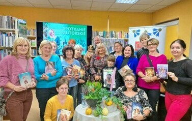 Pisarka stoi otoczona Paniami ze spotkania, kt&oacute;re trzymają zakupione książki autorki