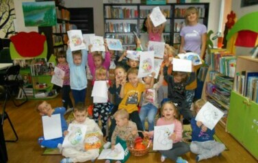 Grupa dzieci trzymająca swoje prace jesienne stoi ze swoimi Paniami i bibliotekarką.