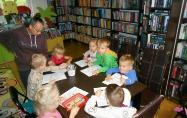 Dzieci siedzą przy stole i kolorują kolorowanki z motywem jesiennym