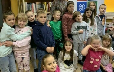 Dzieci stoją w grupie razem ze swoją wychowawczynią w bibliotece w Zblewie.