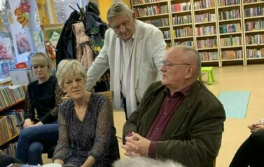 Jeden z czytelnik&oacute;w stoi oparty o krzesła przy kt&oacute;rych siedzą słuchacze i i słucha co m&oacute;wi Pan po prawej stronie.