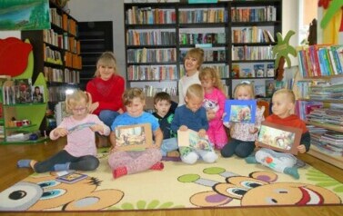 Dzieci siedzą na dywanie ze swoją Panią i Panią z biblioteki.