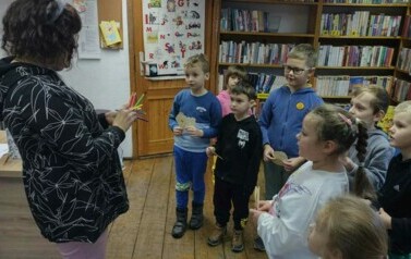 Dzieci stoją naprzeciwko Pani Pedagog, kt&oacute;ra trzyma w rękach kredki. Dzieci zaś trzymają swoje wydarte z papieru serduszka.