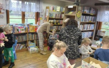 Dzieci stoją w rozsypce, każde dziecko ma starą kartkę od książki i pr&oacute;bują obrywać ją tak aby powstało serduszko. Pani nauczycielka i Pani pedagog pomagają to dzieciom zrobić.