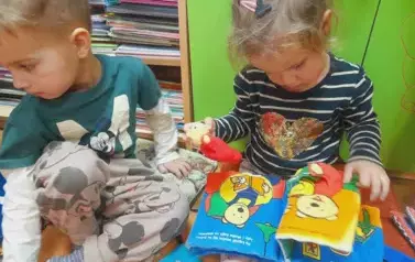 Dziewczynka ogląda książeczkę pluszową, obok niej siedzi chłopiec.