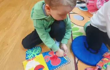 Chłopiec siedzi na podłodze i bawi się pluszową książeczką.