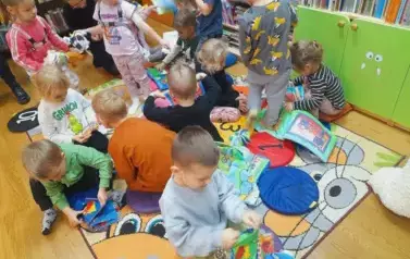Dzieci siedzą na dywanie i bawią się pluszowymi książeczkami.