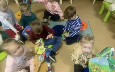 Dzieci siedzą  na siedziskach  w bibliotece i bawią się pluszowymi książeczkami.