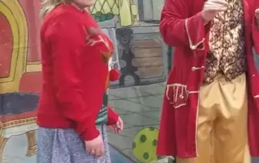 Na tle wnętrza pałacu stoi Pani przebrana za renifera koło dworzanina w białych włosach w czerwonym smokingu i złotych spodniach.