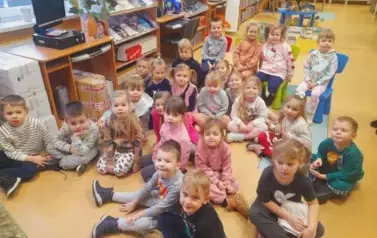 Dzieci siedzą  na siedziskach i słuchają bajki.