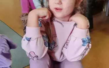Dziewczynka siedzi na siedzisku i recytuje werszyk o babci, w tle są inne dzieci.