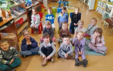 Dzieci siedzą na siedziskach w bibliotece i słuchają bajki.