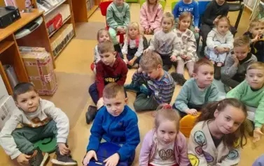 Grupa dzieci siedzi na siedziskach i słucha bajki