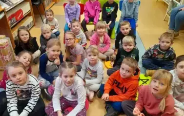 Grupa dzieci siedzi na siedziskach i słucha bajki