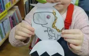 Dziewczynka w jasnych włosach pokazuje swojego pokolorowanego dinozaura.