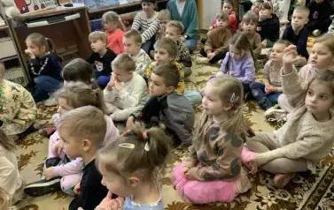 W bardzo licznej grupie siedzą dzieci na dywanie i patrzą na przedstawienie.