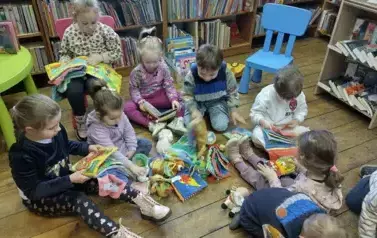 Dzieci siedzą na siedziskach i bawią się pluszowymi książeczkami.