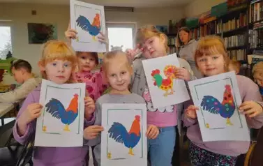 Pięć dziewczynek pokazuje swoje obklejone plasteliną na kartkach kolorowe koguciki.