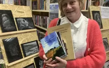 Przy stojaku z obrazami z granitu stoi Czytelniczka z zakupionymi ksiażkami i się uśmiecha.