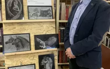 Pan Maciej Syropolski pokazuje wystawione na stojaku piękne obrazy z granitu.