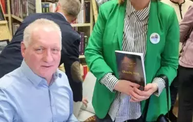 Janusz Szalewski podpisuje książkę uśmiechniętej Pani w zielonej marynarce.