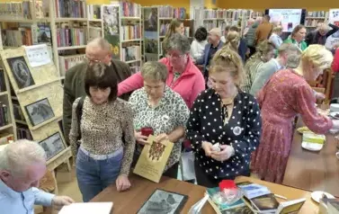 Autor siedzi przy biurku, a do Niego podchodzą Czytelnicy z zamiarem kupienia książki i nabycia autografa. 