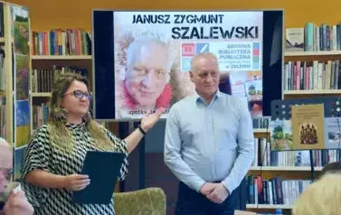 Kierowniczka biblioteki przedstawia Czytelnikom poetę i pisarza Janusza Szalewskiego. Za nimi wisi duży ekran z wyświetlonym plakatem dotyczącym spotkania.