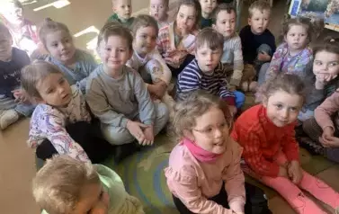 Dzieci siedzą na dywanie i słuchają bajki jaką czyta im bibliotekarka. 
