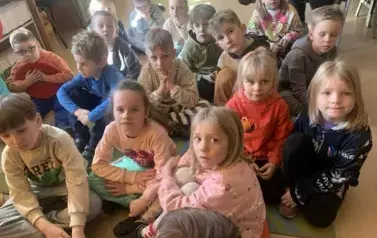 Dzieci siedzą na dywanie i siedziskach i patrzą na bibliotekarkę, kt&oacute;ra im opowiada o książce i o baśniach Andresena.