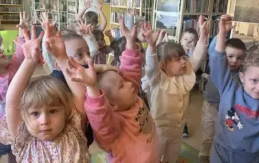 Dzieci stoją w rozsypce i mają wyciągnięte ręce w g&oacute;rze.