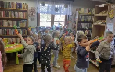 Dzieci trzymając swoje zrobione z papieru marchewki tańczą do piosenki 'Marchewkowe pole"
