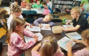 Dzieci przy stołach uzupełniają kredkami karty pracy.