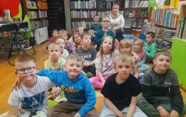 Dzieci siedzą na dywanie i słuchają bajki.