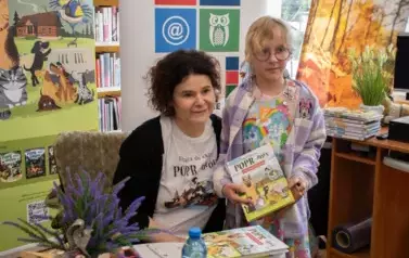 Dziewczynka w blond włosach i okularach stoi blisko pisarki trzymając zakupioną książkę.