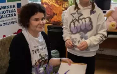 Przy stoliku Anny Sakowicz stoi dziewczynka w warkoczykach z zamiarem kupienia książeczki. Anna Sakowicz podpisuje na książce dedykację.
