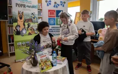 Dzieci stoją przy stoliku Anny Sakowicz z zamiarem kupienia książeczki.